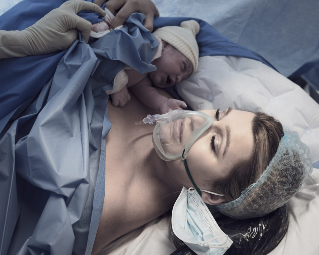Femme après l'accouchement par cesarienne avec masque sur le visage et enfant dans les bras
